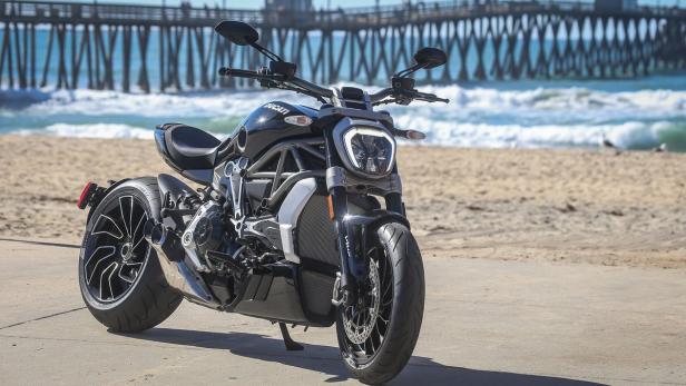 Eine schwarze Ducati Diavel steht am Strand vor einer Seebrücke.