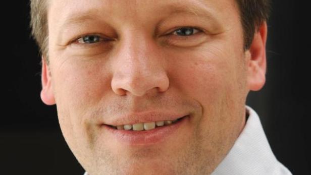 Ein lächelnder Mann mit hellbraunen Haaren und einem hellblauen Hemd.