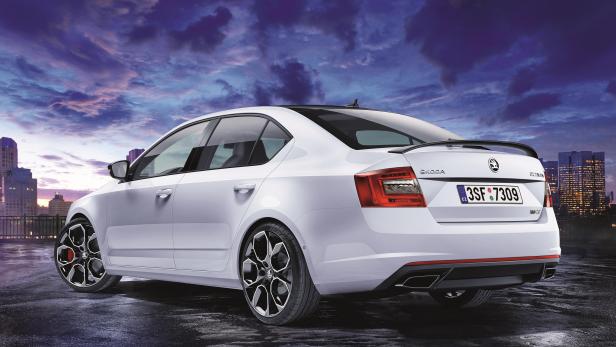 Ein weißer Škoda Octavia mit Heckspoiler vor einer Skyline bei Dämmerung.