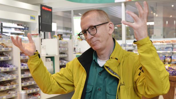 Ein Mann mit Brille und gelber Jacke gestikuliert in einem Geschäft.