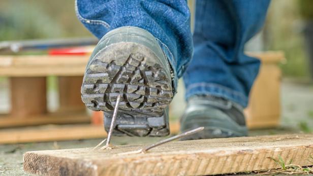 Ein Stiefel tritt auf ein Brett mit einem Nagel.
