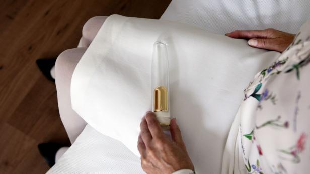 Eine Frau hält ein transparentes Gefäß mit einem goldenen Einsatz in der Hand.