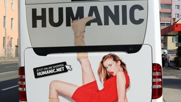 Ein Bus mit einer Werbung für Humanic, die eine Frau in einem roten Kleid und Stiefeln zeigt.