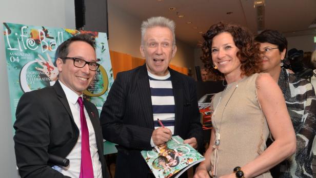 Jean Paul Gaultier signiert ein Life Ball Magazin, umgeben von zwei Personen.