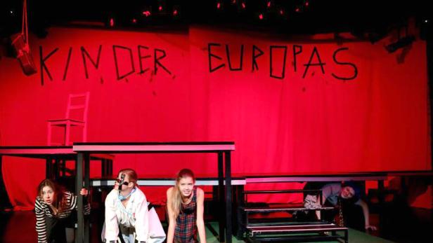 Eine Theaterszene mit dem Titel „Kinder Europas“ im roten Bühnenlicht.