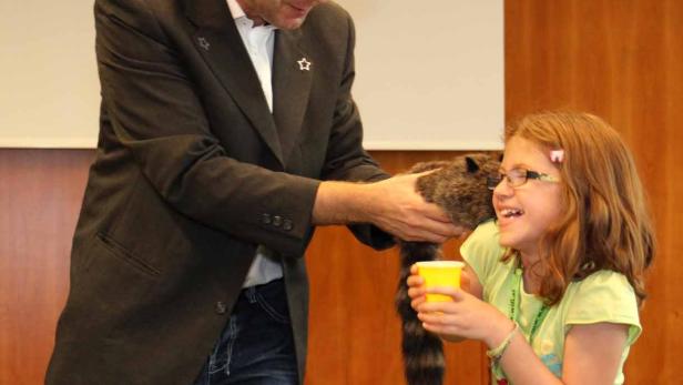 Ein Zauberer mit Zylinder präsentiert einem Mädchen einen Waschbären.