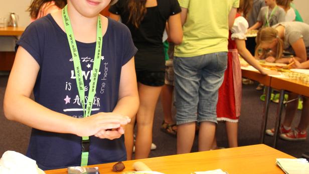 Ein Mädchen formt Pralinen auf einem Tisch, an dem weitere Kinder arbeiten.