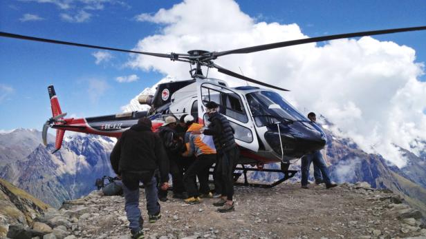 Ein Hubschrauber landet in einer Bergregion, während Menschen ein- und aussteigen.