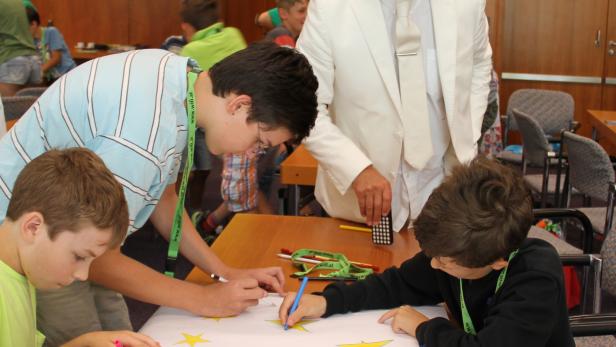 Kinder malen mit einem Mann im weißen Anzug eine Europaflagge.