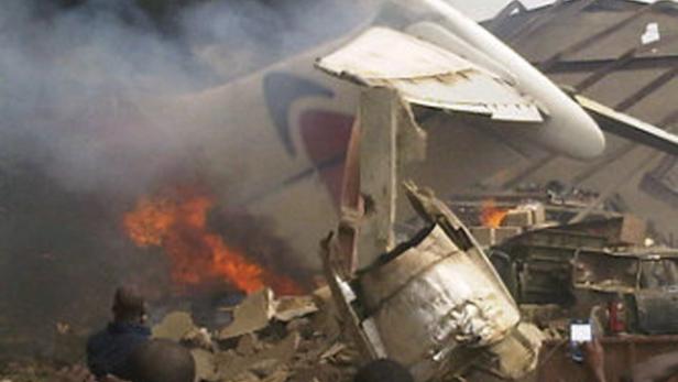 Ein Flugzeugwrack brennt und raucht, während Menschen in der Nähe stehen.