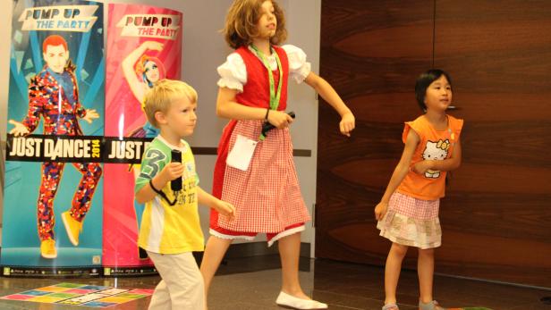 Drei Kinder tanzen vor Postern für das Spiel „Just Dance“.