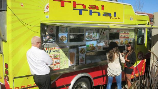 Ein gelber Imbisswagen mit der Aufschrift „Thai Thai Truck“ wird von Kunden frequentiert.