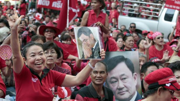 Eine Menschenmenge in roten Hemden demonstriert mit Bildern von Thaksin Shinawatra.