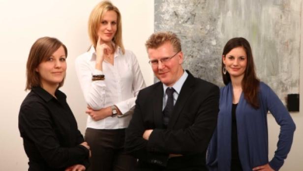 Ein formelles Gruppenfoto von vier Personen vor einem abstrakten Gemälde.