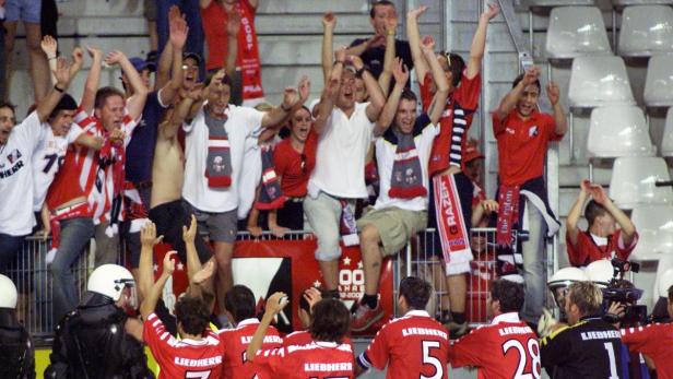 Fußballfans jubeln auf der Tribüne, während Polizisten im Vordergrund stehen.