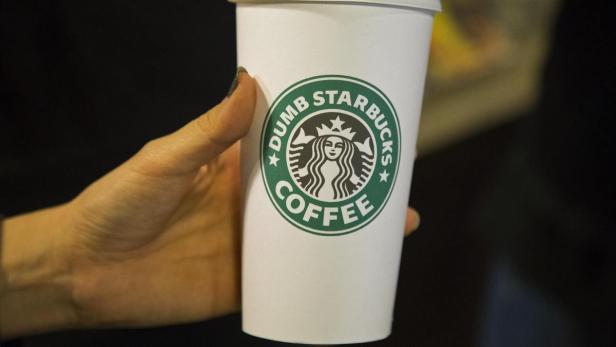 Eine Hand hält einen Starbucks-Kaffeebecher mit dem Aufdruck „Dumb Starbucks Coffee“.