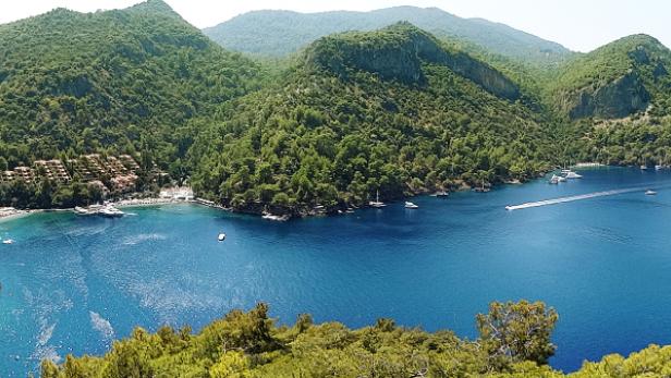 Blick auf eine Bucht mit blauem Wasser, bewaldeten Hügeln und einem Hotelresort.