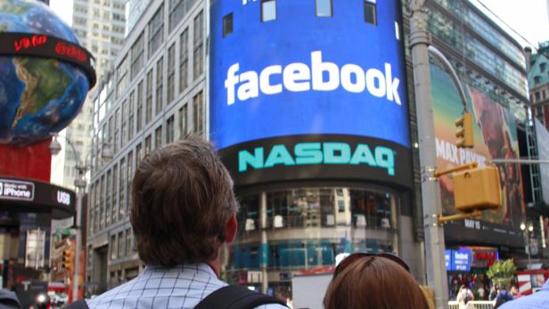 Zwei Personen stehen vor einer großen Werbetafel von Facebook und NASDAQ in New York.