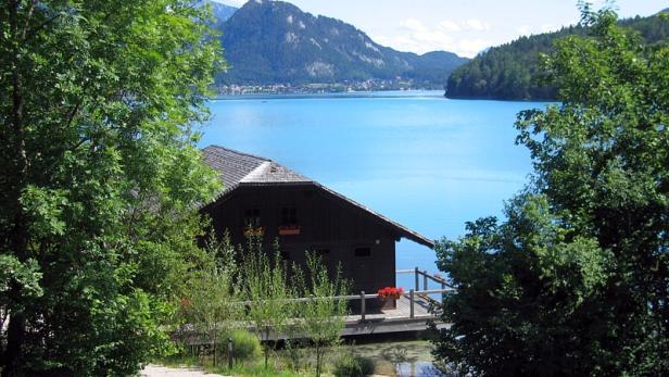 Ein Bootshaus am Ufer eines Sees mit Bergen im Hintergrund.
