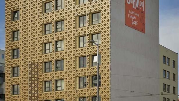 Ein modernes Hotelgebäude mit einer Fassade aus einem Lochmuster und eine rote Straßenbahn davor.