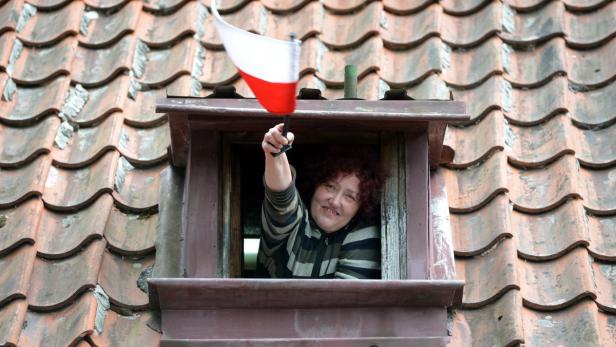Eine Frau winkt mit einer polnischen Flagge aus einem Dachfenster.