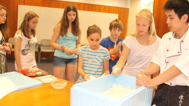 Eine Gruppe Jugendlicher lernt von einem Koch, wie man Sushi zubereitet.