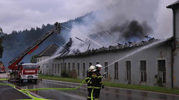 Feuerwehrleute bekämpfen einen Brand in einem Gebäude mit Drehleiter und Wasserschläuchen.