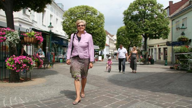 Eine Frau geht auf einer belebten Straße entlang, im Hintergrund eine Familie.