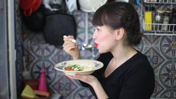 Eine Frau isst eine Suppe mit Gemüse in einer Küche.