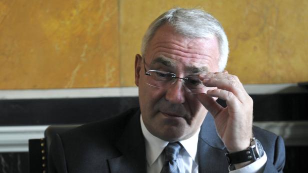 Ein Mann mit Anzug und Brille blickt nach unten und berührt seine Brille.