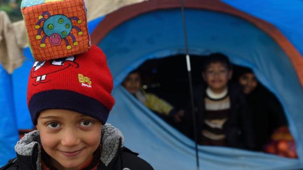 Children pose in a makeshift camp at the Greek-Macedonian border, on March 12, 2016, near the Greek village of Idomeni, where thousands of refugees and migrants are stranded by the Balkan border blockade. More than 14,000 mainly Syrian and Iraqi refugees including many children are camped out at the squalid camp where they have been stranded by Skopje&#039;s decision to close the frontier. Days of heavy rain have turned Greece&#039;s Idomeni border camp into a foul-smelling bog, exposing migrant children to raw sewage, noxious fumes and bitter cold, with aid workers describing conditions as &quot;critical&quot;. / AFP PHOTO / DANIEL MIHAILESCU