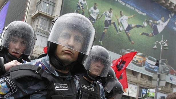 Polizisten in Schutzausrüstung stehen vor einem Werbeplakat in der Stadt.