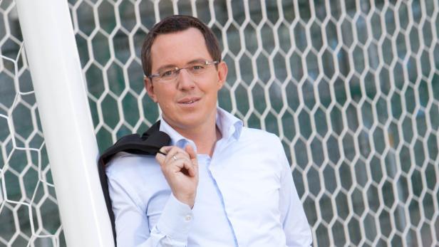 Ein Mann mit Brille und Hemd lehnt an einem Fußballtor.