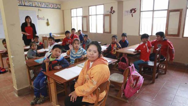 Eine Lehrerin steht vor einer Klasse von Kindern in einem Klassenzimmer.
