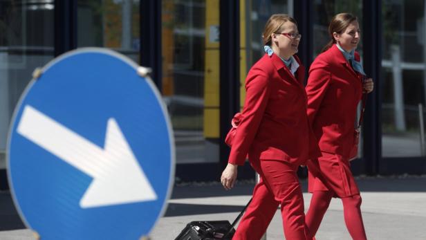 Zwei Stewardessen in roten Uniformen gehen an einem blauen Richtungsschild vorbei.