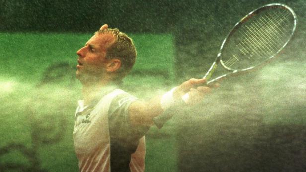 Ein Tennisspieler steht im Regen und hält einen Schläger hoch.
