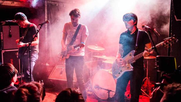 Eine Band spielt live auf einer Bühne mit roter und weißer Beleuchtung.