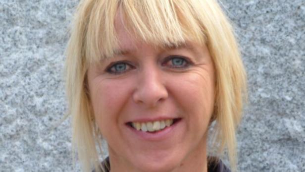 Porträt einer lächelnden Frau mit blonden Haaren und blauen Augen.