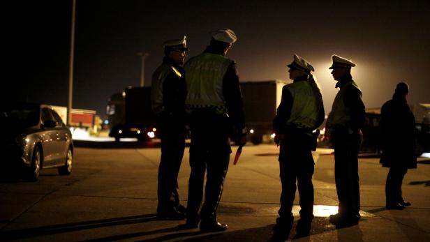 Mehrere Polizisten stehen nachts auf einem Parkplatz vor einem LKW und einem Auto.