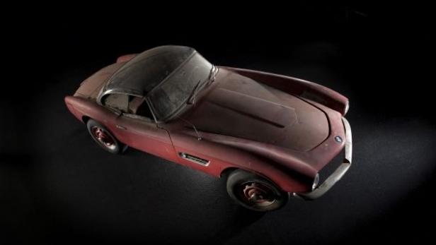 Ein verstaubter, roter BMW 507 steht in einem dunklen Raum.