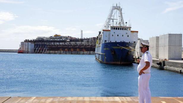 Ein Mann in Marineuniform steht vor dem teilweise versunkenen Kreuzfahrtschiff Costa Concordia.