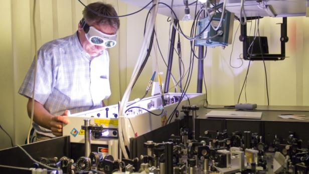 Ein Mann mit Schutzbrille arbeitet an einem komplexen optischen Gerät.
