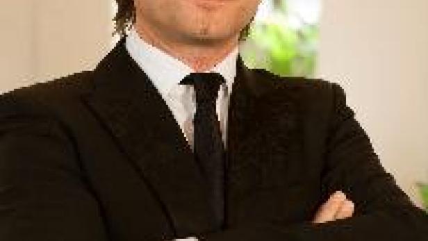 Ein Mann mit verschränkten Armen in einem schwarzen Anzug und Krawatte.