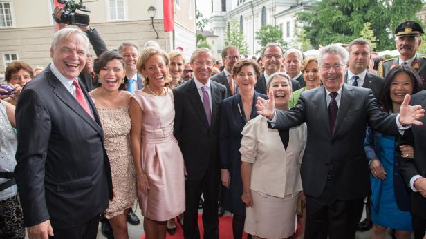 Eine Gruppe von Menschen posiert lachend auf einem roten Teppich vor einem Gebäude in Salzburg.