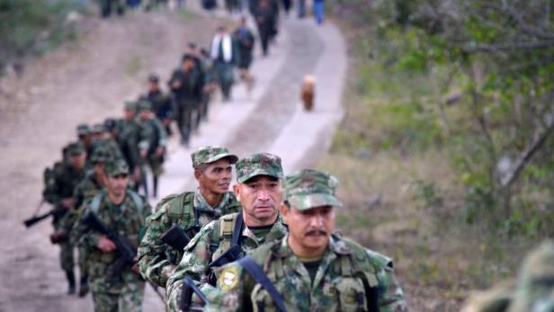 Viele FARC-Rebellen in Tarnanzügen mit Tarnkappe die hintereinander eine Straße entlang marschieren