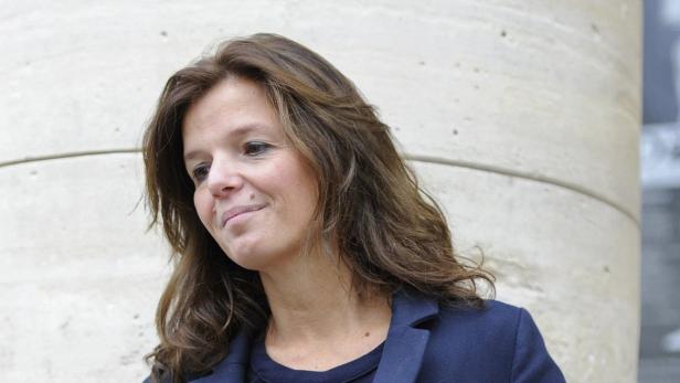 Eine Frau mit braunen Haaren und einem blauen Blazer vor einer hellen Wand.