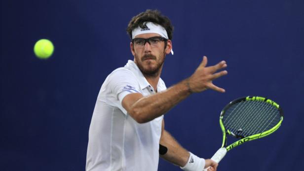 Ein Tennisspieler mit Brille und Stirnband schlägt einen Ball.