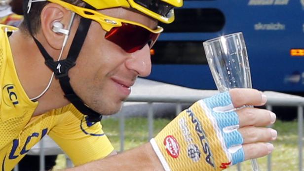 Vincenzo Nibali mit gelbem Trikot und Helm hält ein Champagnerglas.