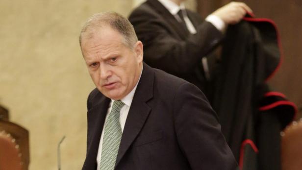 Ein Mann in einem dunklen Anzug und einer hellgrünen Krawatte blickt aufmerksam zur Seite.