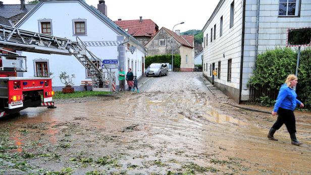 Eine überflutete Straße in Pöchlarn mit Schlamm und einer Frau, die durch das Wasser geht.